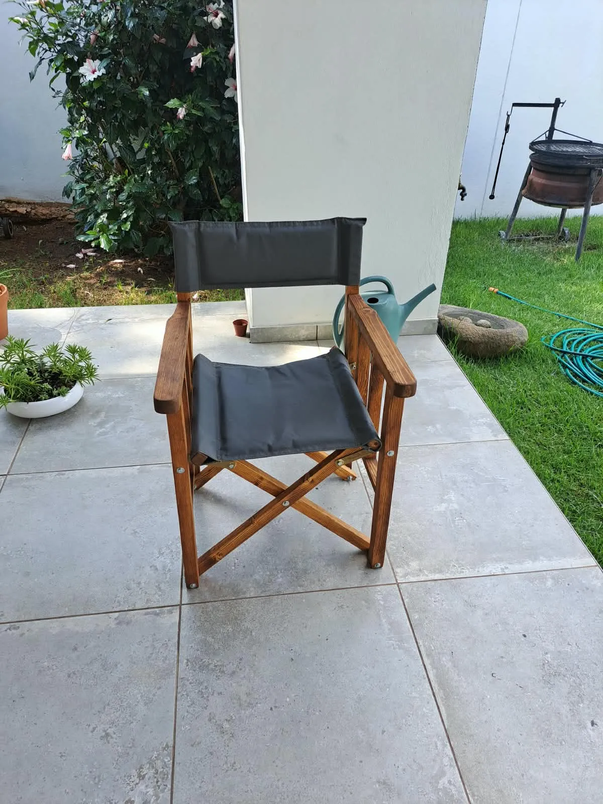 A folding timber director's chair with a dark grey canvas seat and back, on a paved patio