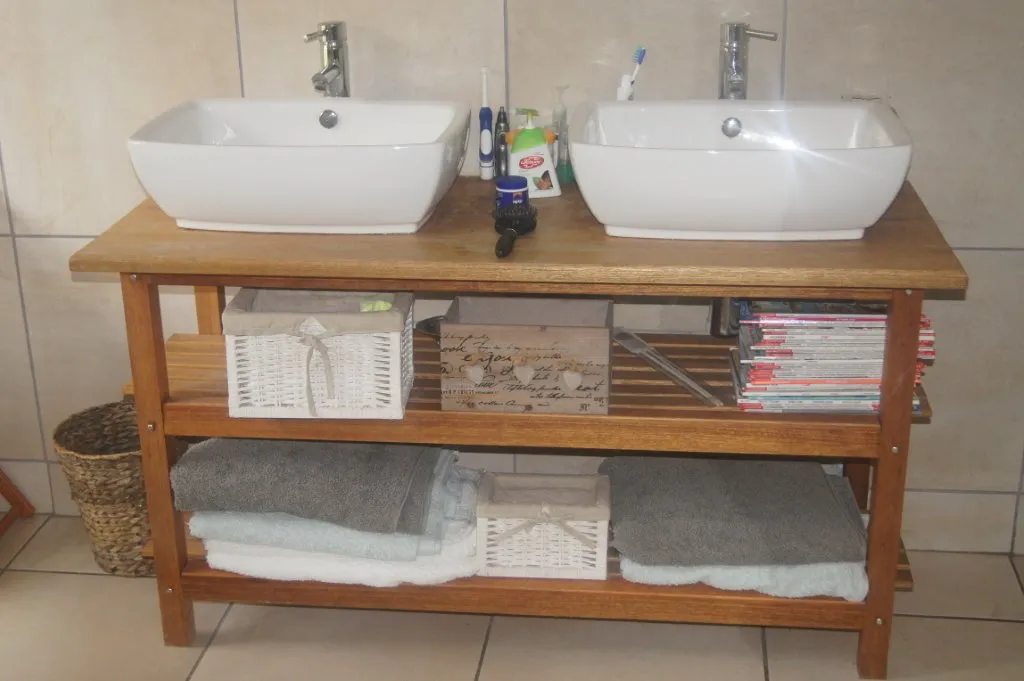 A timber table holding two white basins, with two slatted shelves for towels and baskets below