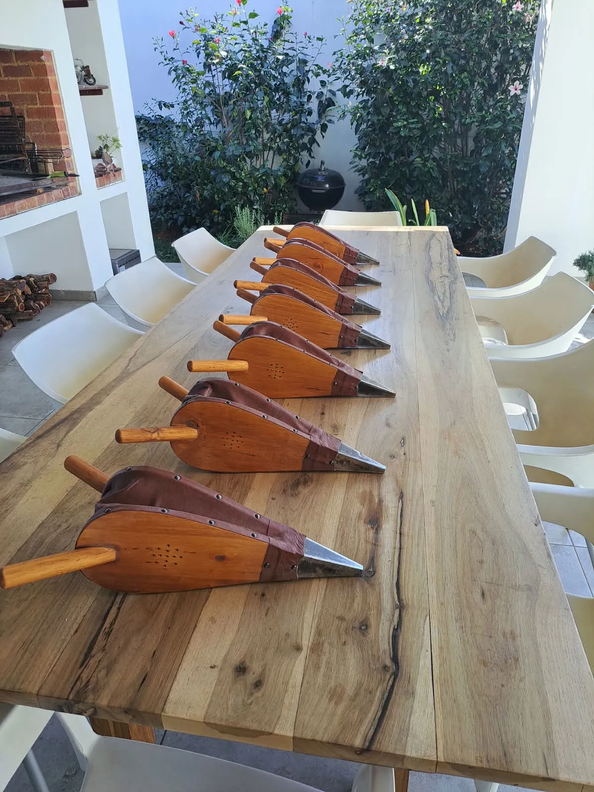 Eight timber and leather fire bellows lined up on a long wooden table