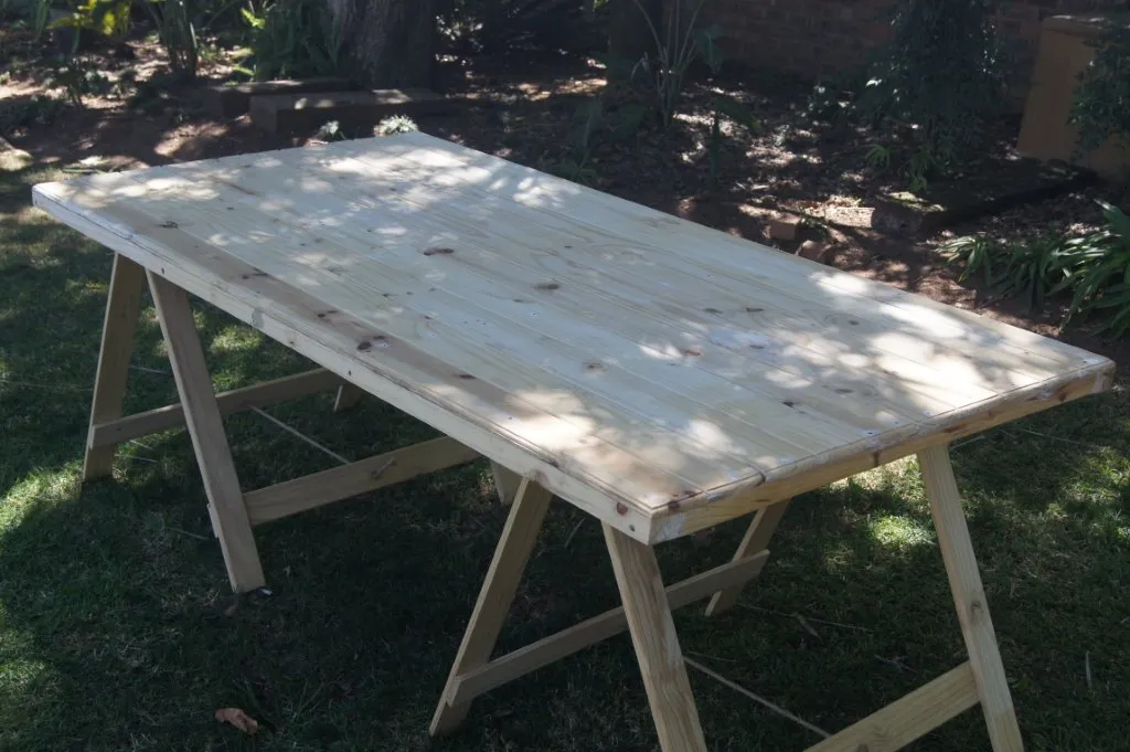 A pine trestle table with a plank top, set up on a lawn