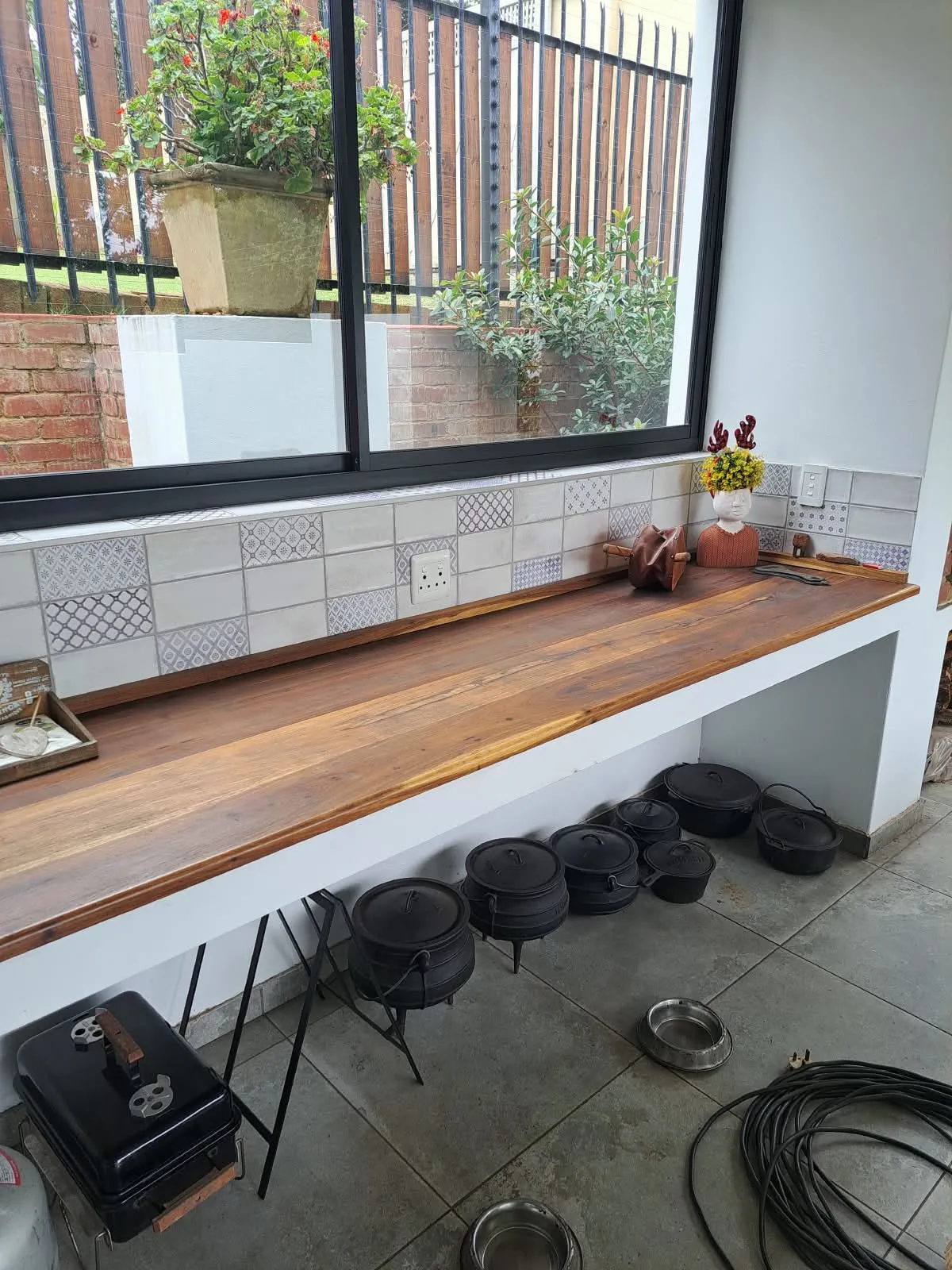 A long hardwood countertop below a window, with a tiled splashback