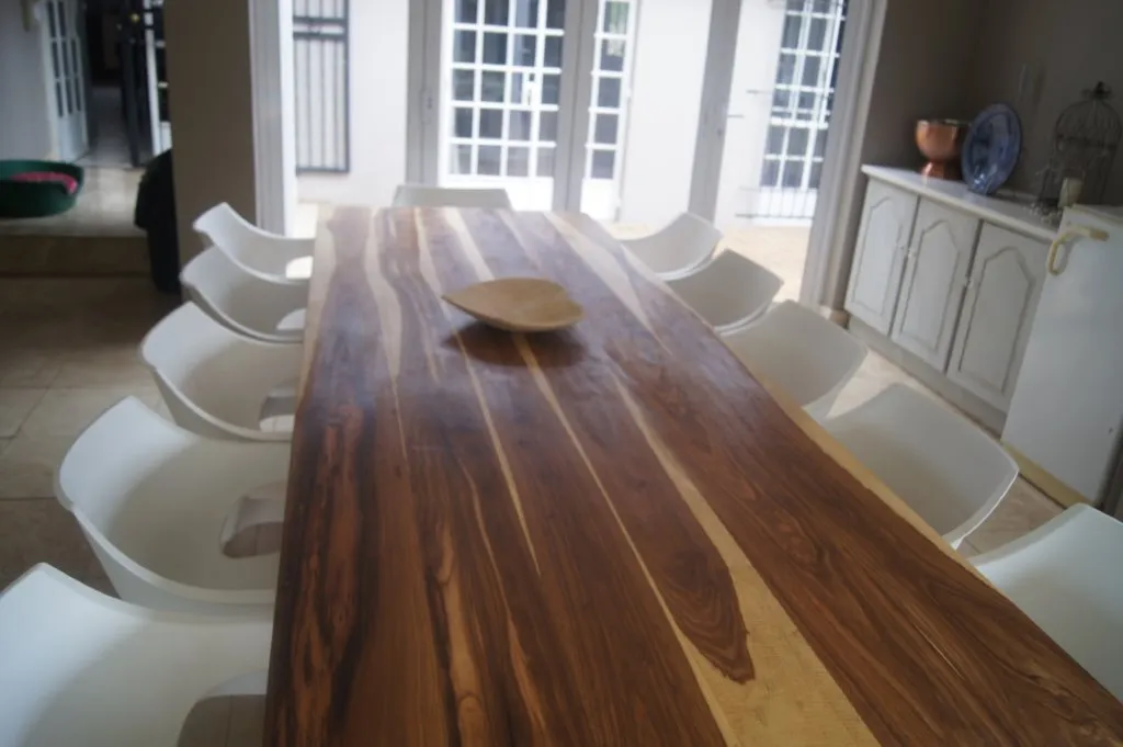 A long hardwood dining table with a rich, dark grain, surrounded by white chairs