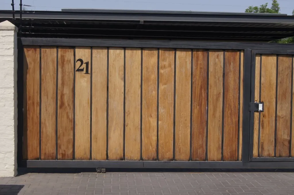 A sliding motor gate clad in vertical timber boards within a black steel frame